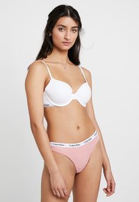 Witte gewatteerde bh met verstelbare bandjes, gecombineerd met een roze en witte gestreepte string met een logo tailleband. Eenvoudig, modern ontwerp.