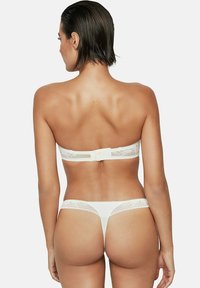 Ensemble de lingerie en dentelle blanche comprenant un soutien-gorge sans bretelles avec une fermeture à crochet et un string assorti, mettant en valeur des détails de dentelle délicats et un tissu lisse.