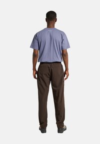 Blauwe korte mouwen T-shirt voor mannen met logo op de achterkant, gecombineerd met bruine broek met een elastische tailleband en zakken. Zwarte schoenen zichtbaar.