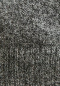 Texturerad grått tyg med en blandning av mörka och ljusa fibrer. Har ett stickat mönster med små variationer i tjocklek och mjukhet.