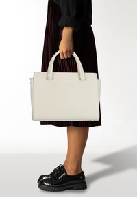 Un bolso estructurado de color gris claro con dos asas superiores, hecho de un material texturizado, que cuenta con herrajes y detalles de costura en plata.