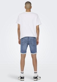 Witte katoenen t-shirt, blauwe denim shorts met opgerolde manchetten, en zwart-witte sneakers met contrasterende strepen. Eenvoudig en casual ontwerp.