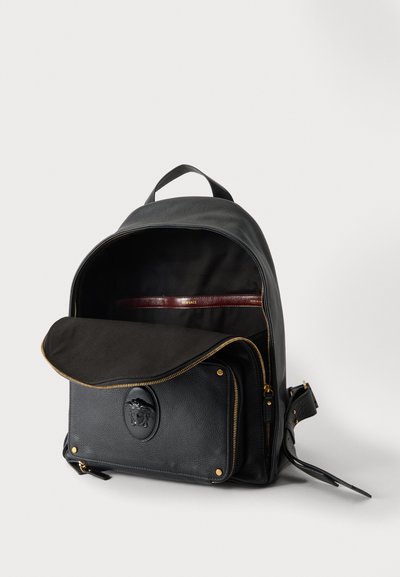 Sac à dos en cuir noir avec compartiment principal ouvert et poche avant zippée arborant un logo Méduse et des détails de fermeture éclair dorés.