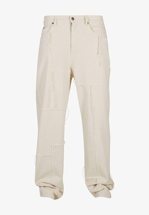 Beige pamut cargo nadrág, több zsebbel, nyers varrási részletekkel, laza fazonnal és feltekert alsóval. Texturált anyag, látható varrásokkal.