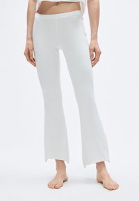 Leggings évasés blancs en tissu doux et extensible, présentant un design épuré avec des ourlets bruts et une taille ajustée.