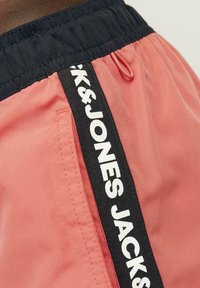 Korte roze shorts met een zwarte elastische tailleband en zijzak. Zwarte zijstreep met "JACK & JONES" in grote witte letters.