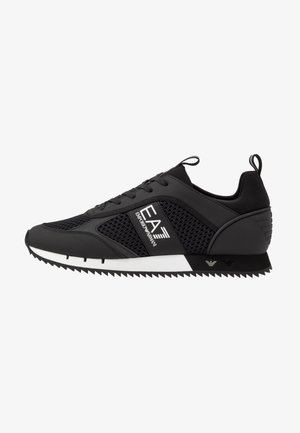 Zapatilla negra con paneles de malla, cordones y una suela de goma blanca. Presenta acentos geométricos y detalles de logotipo en el lateral. Acabado texturizado.