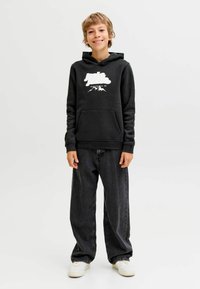 Sudadera negra con capucha, impresión de montaña blanca y logo, bolsillo delantero, combinada con jeans oscuros de corte suelto y zapatillas blancas.