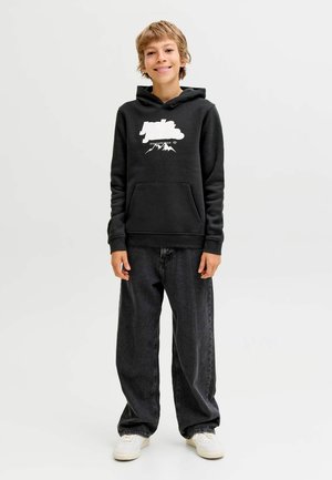 Črna kapuca sweatshirt z belim tiskanjem gora in logotipa, sprednji žep, združena z ohlapnimi temnimi kavbojkami in belimi športnimi copati.