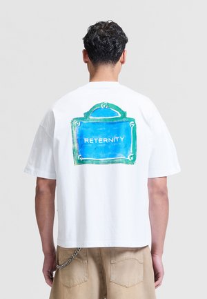 Mand med kort mørkt krøllet hår iført en hvid t-shirt med et blåt og grønt grafisk tegn mærket "RETERNITY" på bagsiden.