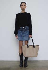 Bolso tote beige con detalles en negro, textura suave, suéter negro, minifalda de mezclilla con dobladillo deshilachado y botas vaqueras negras.