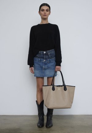 Beige tote bag with black accents, smooth texture, black sweater, denim miniskirt with frayed hem, and black cowboy boots.