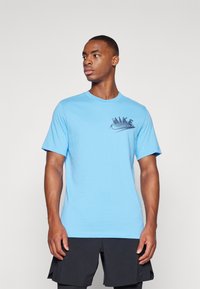 T-shirt in cotone blu chiaro con maniche corte, scollo rotondo e logo Nike nero sul petto. Texture liscia, design aderente.