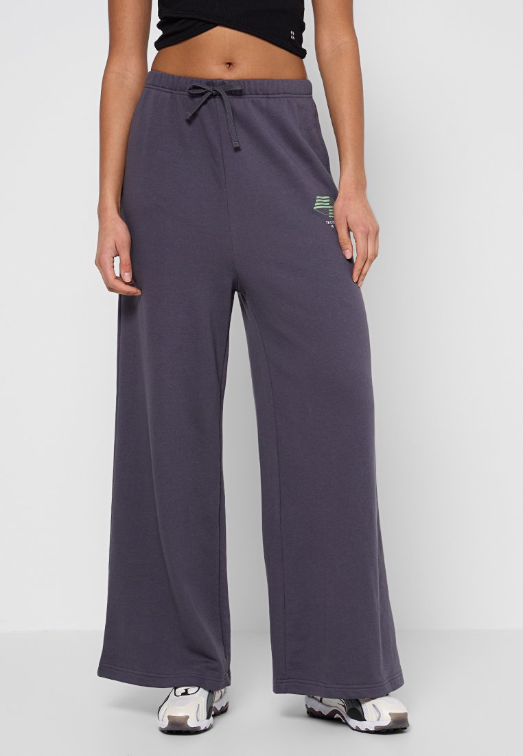 Grey wide-leg sweatpants made of soft cotton blend fabric, featuring an elastic waistband with drawstring and a small green logo detail.