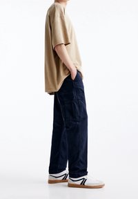 Beige katoenen t-shirt, losse fit met korte mouwen, gecombineerd met donkerblauwe cargobroeken met meerdere zakken, afgewerkt met witte sneakers.