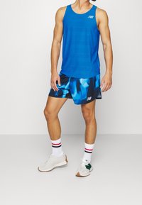 Blå ärmlös tanktop med ett strukturerat randmönster, i kombination med flerfärgade shorts med blå och svarta abstrakta mönster. Vita sneakers.