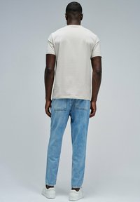 Camiseta de manga corta color beige claro combinada con jeans de mezclilla azul claro. Los jeans tienen un corte holgado con costuras visibles en los bolsillos traseros, llevados con zapatillas blancas.