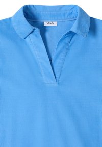 Polo bleu clair avec col et ouverture en V, présentant une étiquette blanche avec le nom de la marque "Cecil" à l'intérieur du col.