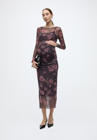 Ένα φόρεμα εγκυμοσύνης από διάφανο μαύρο ύφασμα με ροζ λουλουδάτο σχέδιο. Εφαρμοστή σιλουέτα, μακριά μανίκια και μήκος μέχρι το γόνατο. Συνδυάζεται με μαύρο φάκελο τσάντας.