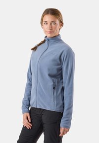 Svetlo modra flis jopica z zadrgo po celotni dolžini, visokim ovratnikom in stranskimi žepi; mehka tekstura s prilegajočo se obliko in vezenim detajlom logotipa.