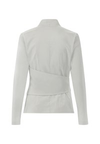 Blusa bianca a maniche lunghe con colletto strutturato, design a strati sul retro e texture liscia, che enfatizza una silhouette aderente.