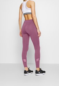 Leggings de sport en rose foncé avec des panneaux en mesh, taille haute et coupe ajustée, associés à des chaussures de sport noires.
