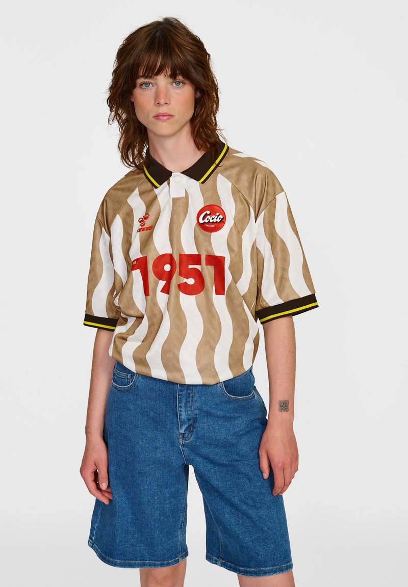 Brun och vit randig kortärmad tröja med svart krage, gula detaljer och röd "1951" tryck. Kombinerad med blå denimshorts.