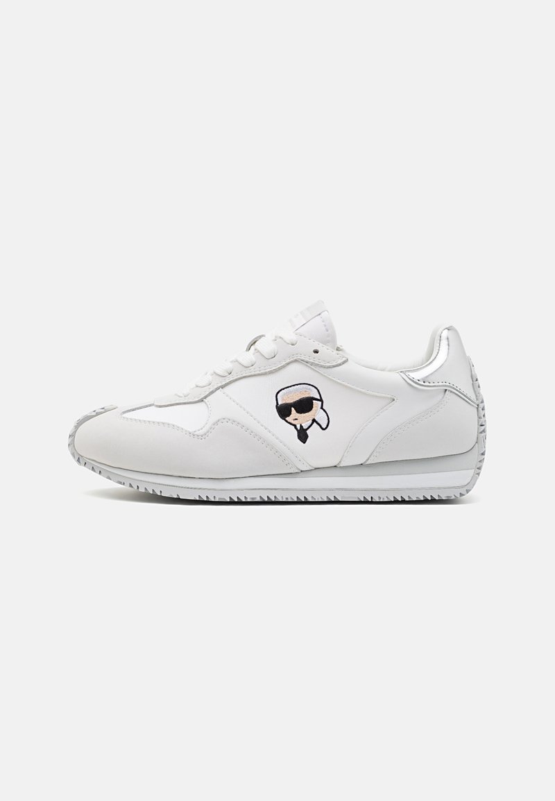 Zapatilla blanca con parte superior de cuero suave, puntera redondeada, logo bordado negro en el lateral y suela de goma texturizada. Costuras de acento sutiles.