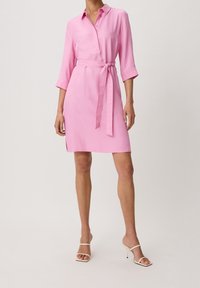Abito rosa con scollatura a colletto, maniche a tre quarti e cintura in vita. Tessuto morbido con una silhouette leggermente aderente.