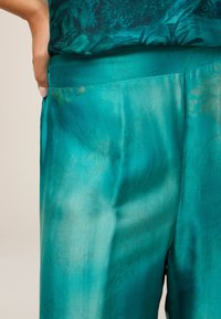 Türkisfarbene Satin-Hosen mit glatter Textur, einem schlichten Bund und einem dezenten floralen Muster in helleren Farbtönen.
