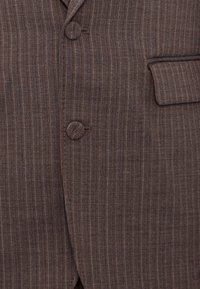 Bruine herringbone colbertstof met verticale streepjes, twee knopen, een enkele zak en een gladde textuur.