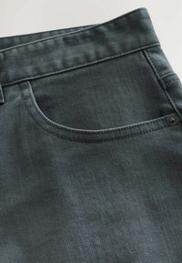 La tela de mezclilla gris oscuro presenta un bolsillo estándar a la izquierda, con costuras visibles y un detalle de botón de metal cerca de la cinturilla.