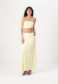 Lemon-yellow two-piece outfit featuring a strapless crop top and a long, fitted skirt. Smooth fabric with a soft texture. High-heeled purple sandals.