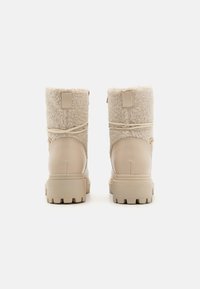 Bottes d'hiver beige en haut en shearling, surface texturée et semelle en caoutchouc renforcée avec un motif à crampons pour une traction optimale.