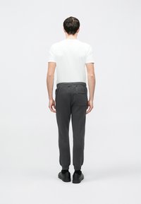 Szürke melegítőnadrág rugalmas derékpánttal, passzés bokarész és hátsó zseb, rövid ujjú fehér pólóval, hátulnézetben.