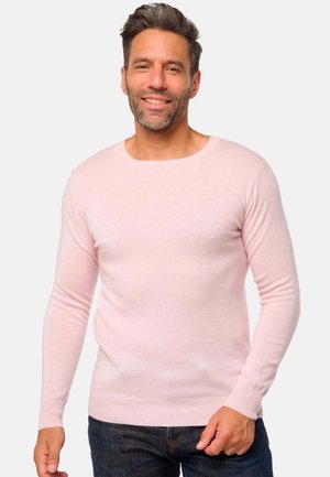 Pull en tricot rose clair avec des manches longues et un col rond. Texture douce et coupe ajustée. Associé à un jean en denim bleu foncé.