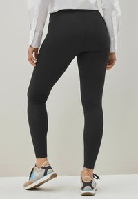 Svarta leggings i stretchigt material med hög midja. Kombinerade med flerfärgade träningsskor, sedd bakifrån.