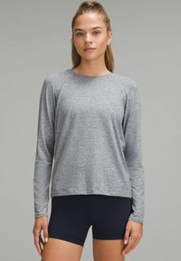 Harmaa pitkähihainen urheilu paita rentoa istuvuutta, raglan-hihat ja pehmeä pinta, yhdistettynä tummansinisiin shortseihin.