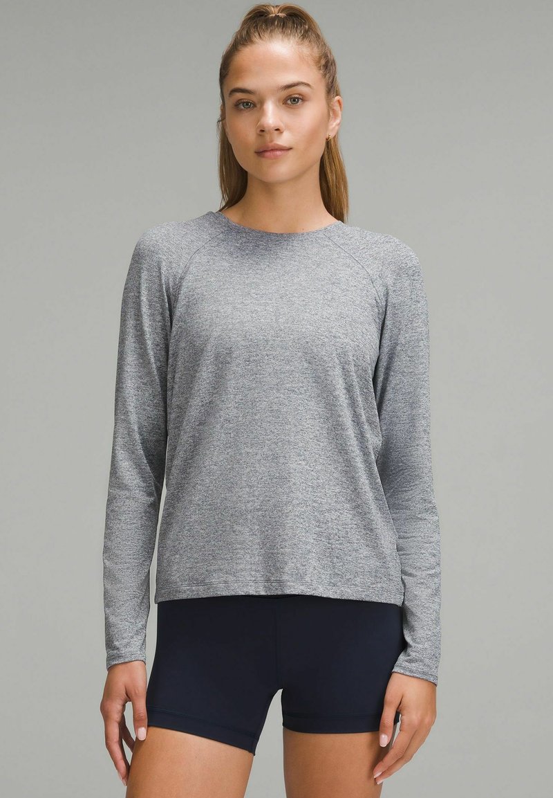 Harmaa pitkähihainen urheilu paita rentoa istuvuutta, raglan-hihat ja pehmeä pinta, yhdistettynä tummansinisiin shortseihin.