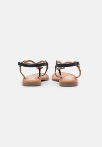 Sandalias planas negras con correas de cuero con bordes ondulados, hebillas ajustables y plantillas beige. Diseño de perfil bajo con una textura suave.