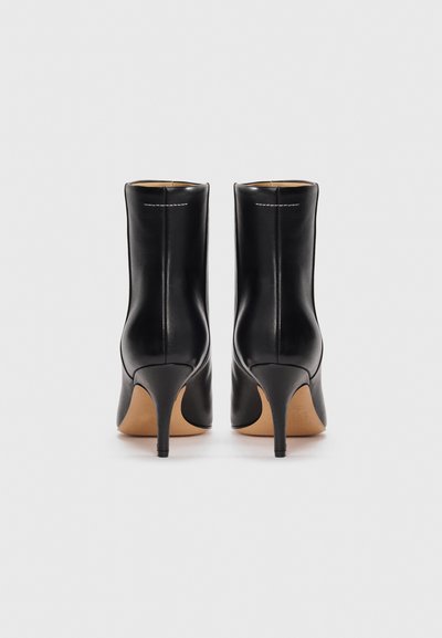Bottines en cuir noir au design élégant, avec un bout pointu et un fin talon haut. Elles présentent une texture lisse et des détails de couture blanche subtile.