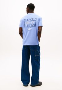 Jasnoniebieska bawełniana koszulka z nadrukiem na plecach oraz ciemnoniebieskie, szerokie jeansy z bocznymi kieszeniami i detalami przeszyć.