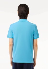 Camisa polo de manga corta con cuello en tejido de color azul brillante. Textura suave con dobladillo recto y sutiles aberturas laterales.