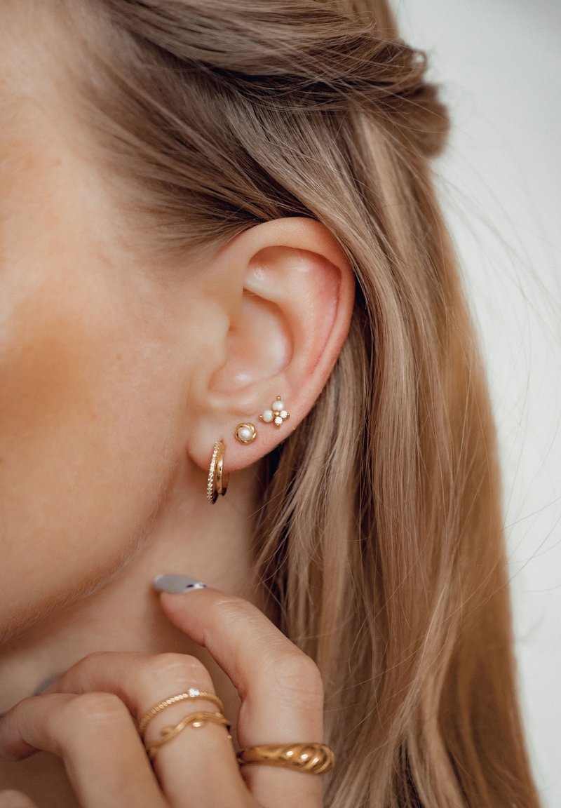 Les boucles d'oreilles en or et perles comprennent un petit anneau, une perle à clous et un design floral avec plusieurs petites perles, sur fond clair.