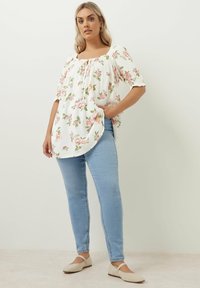 Vit blommig topp med rosa rosor och gröna blad, med fyrkantig halsringning och korta puffärmar, kombinerad med ljusblå skinny jeans.