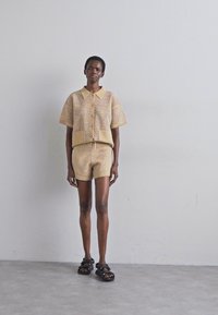 Light yellow knitted two-piece set featuring a short-sleeve collared top with button closure and matching shorts, paired with black sandals.