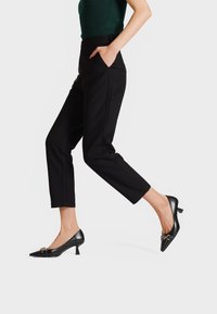 Décolleté neri con tacco alto, punta affusolata, dettagli in metallo dorato, finitura in pelle liscia e tacco corto e sottile. Indossati con pantaloni neri.