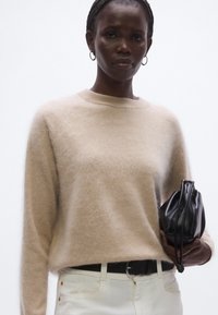 Beżowy, miękki wełniany sweter z okrągłym dekoltem i długimi rękawami, zestawiony z białymi spodniami i czarną torbą na sznurku. Gładka faktura, luźny krój.