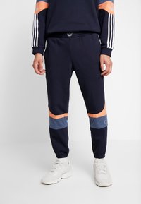 Marina joggers med ljusorange och blå meshpaneler. Har en elastisk midja och ribbade muddar. Tillverkade av mjukt, andningsbart material.