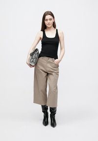 Black tank top, beige wide-leg pants, and knee-high black boots. Holding a textured black and white snake-patterned clutch. Simple background.